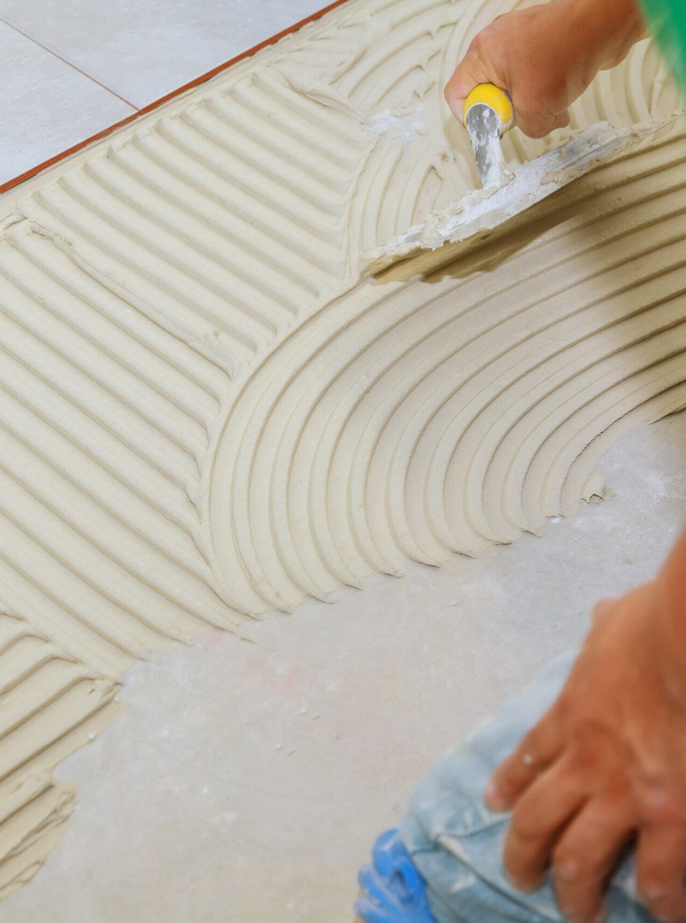 Master puts adhesive Spreading wet mortar before applying tiles on bathroom floor.